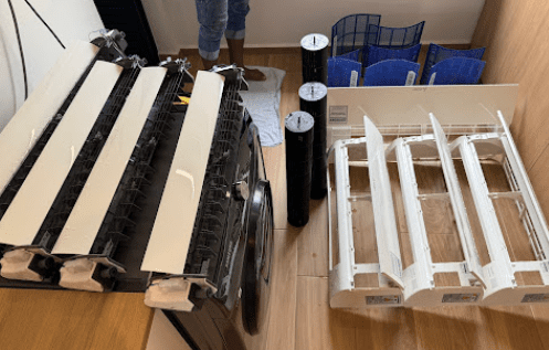 The photo shows disassembled aircon parts laid out neatly on the floor for deep cleaning and maintenance.