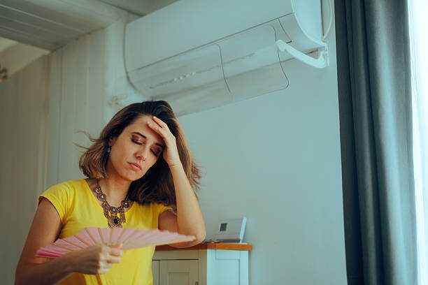 A woman feeling hot under an aircon, fanning herself—signs something is wrong with your aircon like weak cooling or poor airflow.