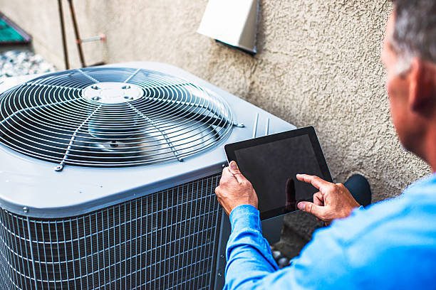 Technician inspecting an outdoor aircon unit using a tablet, representing high-quality aircon servicing in Singapore with precise diagnostics, efficient maintenance, and professional expertise.